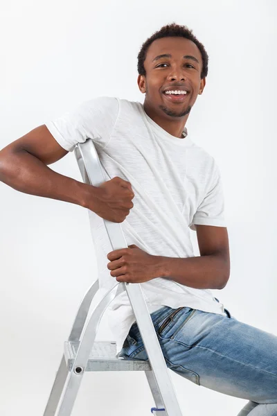 Sonriente hombre afroamericano en camiseta blanca y jeans está sentado en la escalera. Concepto de reparador y gente de clase trabajadora . — Foto de Stock