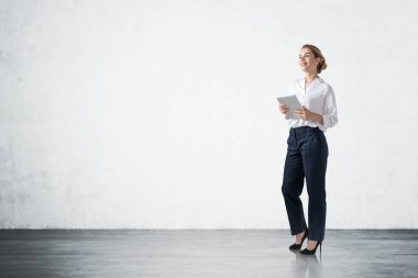 Beton duvarın yanında tablet bilgisayarla duran gülümseyen genç iş kadınının portresi. Planlama kavramı. Model