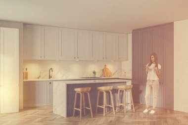 Modern mutfakta, beyaz ve gri duvarları, ahşap zemini, barı ve dolapları olan genç ve güzel bir kadın. Renkli resim çift pozlama