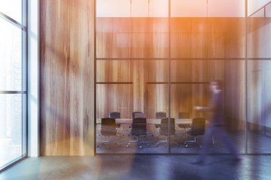 Blurry young businessman walking in modern meeting room with wooden walls, concrete floor and long conference table. Toned image