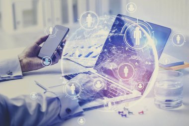 Bulanık ofiste bilgisayar ve akıllı telefon kullanan iş adamlarının elleri HR arayüzü ve gezegen hologramına çifte maruz kalıyor. Tonlanmış görüntü. Bu görüntünün elementleri NASA tarafından desteklenmektedir