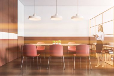 Modern yemek odasında beyaz ve ahşap duvarları, ahşap zemini ve kırmızı sandalyeli uzun masası olan genç bir kadın. Tonu ayarlanmış resim