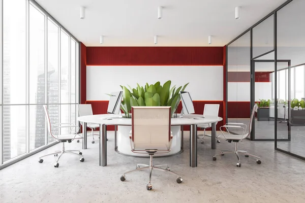 Front view of modern open space office with white and red walls, concrete floor and round computer table. 3d rendering