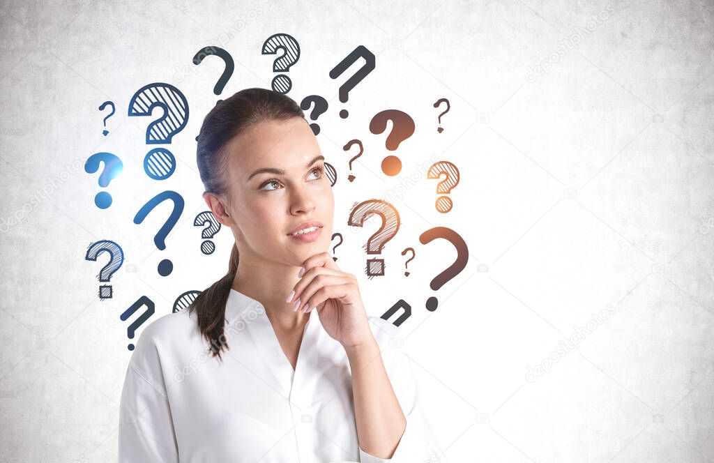 Portrait of thoughtful young woman standing near concrete wall with question marks drawn on it. Mock up