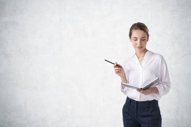 Planlayıcı ve kalemle beton duvarın yanında duran genç bir iş kadınının portresi. Planlama ve evrak işleri kavramı. Model