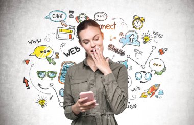 Akıllı telefonlu düşünceli genç bir kadın beton duvarın yanında duruyor. Üzerinde renkli sosyal medya çizimleri var..