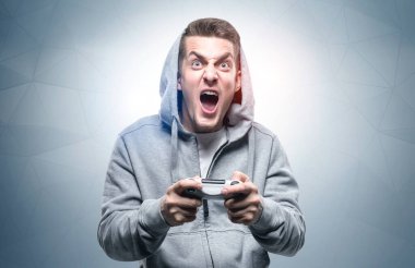 Kapüşonlu genç bir adamın portresi bağırıyor ve kumandasını gri duvarın yanında tutuyor. Oyun anlayışı ve güçlü duygular