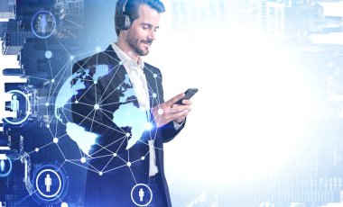 Bulanık şehirde akıllı telefon ve kulaklık kullanan neşeli genç iş adamı. Gezegen ve HR ağ arayüzü iki katına çıkıyor. Görüntünün tonlandırılması. Bu görüntünün elementleri NASA tarafından desteklenmektedir.