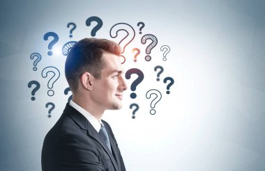 Üzerinde soru işaretleri olan gri duvarın yanında duran genç işadamının yan görüntüsü. Model