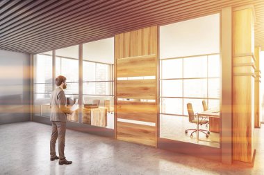 Gri ve ahşap duvarları ve arka planda açık uzay ofisi olan modern ofis salonunda belgeleri olan genç bir işadamı. Tonu ayarlanmış resim