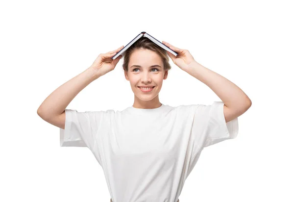 彼女の頭の上に本で立っている白いTシャツの中に笑顔若い女性の孤立した肖像画 — ストック写真