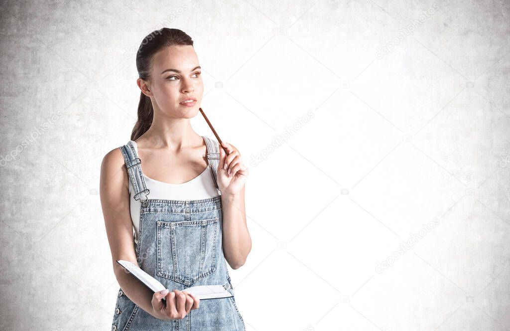 Portrait of pensive young woman holding books near concrete wall. Concept of education. Mock up