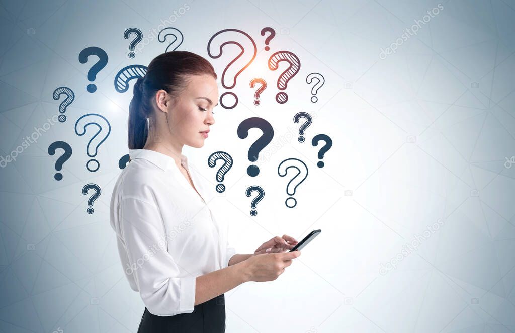 Side view of serious young businesswoman using smartphone near gray wall with question marks drawn on it. Mock up