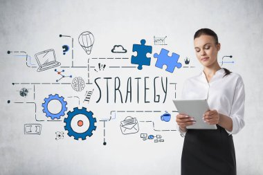 Üzerinde iş stratejisi çizimi olan beton duvarın yanında duran tabletli genç bir iş kadını.