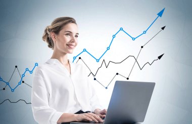 Üzerinde grafikler olan gri duvarın yanında dizüstü bilgisayar kullanan gülümseyen genç iş kadınının portresi. Yatırım ve mali başarı kavramı