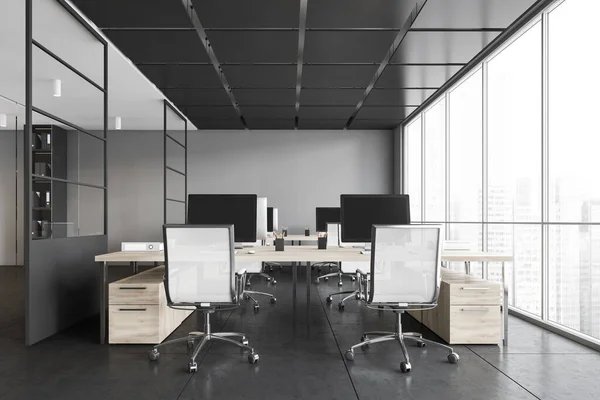 Grey office room with armchairs and computers on the tables near windows. Dark office room with modern wooden minimalist furniture on tiled floor, 3D rendering no people