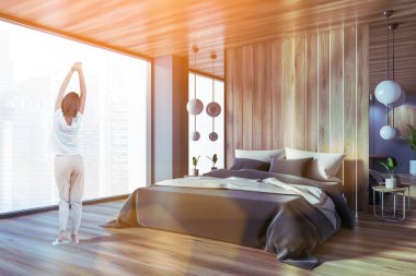 Ana yatak odasında, gri ve ahşap duvarları, ahşap zemini ve rahat kral yatağı olan genç bir kadının dikiz görüntüsü. Tonu ayarlanmış resim