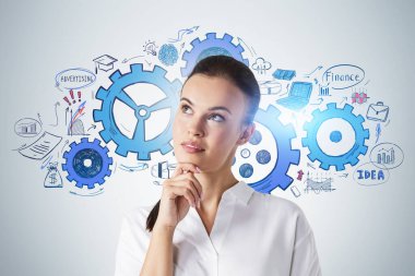 Üzerinde çizimler olan gri duvarın yanında duran düşünceli genç iş kadını portresi.