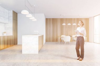 Modern mutfakta tahta ve beyaz duvarları, beton zemini ve yemek masası olan genç bir kadın. Tonu ayarlanmış resim
