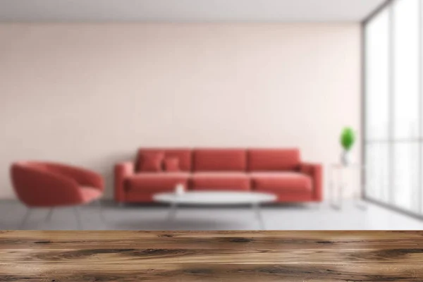 Wooden table for your product standing in blurry living room with pink walls, concrete floor, red sofa and armchair standing near round coffee table. 3d rendering