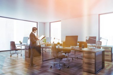 Beyaz duvarları, ahşap zemini ve sıra sıra bilgisayar masaları olan modern açık uzay ofisinde çalışan genç bir işadamı. Tonu ayarlanmış resim