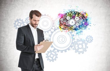 Üzerinde renkli beyin çizimi olan beton duvarın yanında duran genç ve ciddi bir iş adamı.