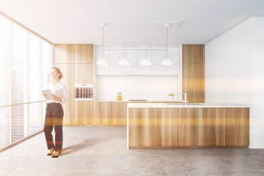 Modern mutfakta tahta ve beyaz duvarları, beton zemini ve barı olan genç bir kadın. Tonu ayarlanmış resim
