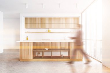 Beyaz ve ahşap duvarlar, beton zemin ve ahşap adayla modern mutfakta yürüyen bulanık genç adam. Tonu ayarlanmış resim