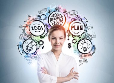 Üzerinde yaratıcı bir çizim olan gri duvarın yanında duran neşeli, kendinden emin genç Avrupalı iş kadını portresi.