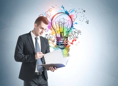 Üzerinde renkli bir çizim olan gri duvarın yanındaki belgeleri okuyan genç işadamının portresi.