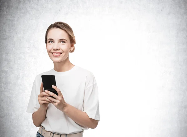 Atrakcyjna Młoda Kobieta Betonowym Tle Trzymająca Smartfona Uśmiechnięta Marząca Przyjemnych — Zdjęcie stockowe