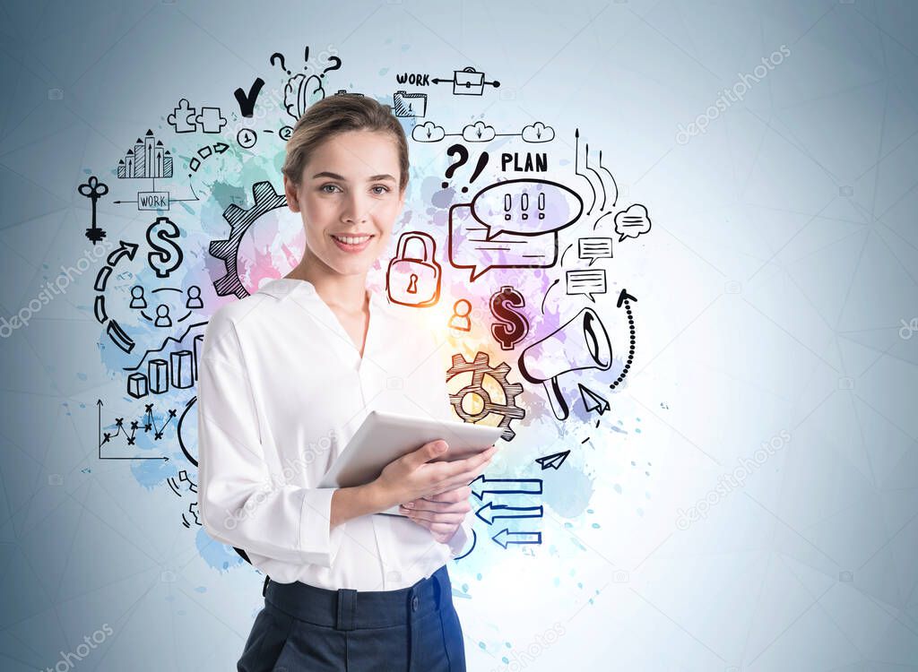 Front view of attractive young woman in formal wear holding a tablet gadget and standing near light blue wall with creative colorful idea and business sketches and doodles drawn on it.
