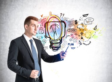 Elinde telefonla beton bir duvardaki renkli ampulün arka planında duran takım elbiseli beyaz bir iş adamı. Yeni fikir kavramı, iş planı