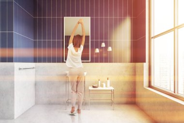 Esmer kız, pijamasını giymiş. Evinin arka tarafında, modern banyonun içinde duruyor. Uyandıktan sonra ellerini uzatıyor.