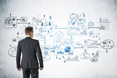 Yaratıcı iş stratejilerine bakan genç iş adamlarının arka görüşü ve beton duvarda zihin haritası şeklinde çizilmiş bir çizim. Geliştirme kavramı, iyi fikir ve yönetim