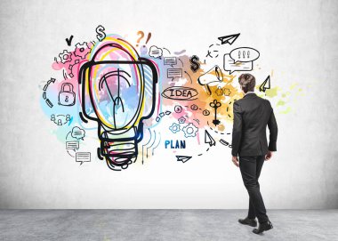 Ofisteki siyah takım elbiseli genç işadamı, büyük ampul, ikonlar, plan ve fikirlerle iş planı skecine bakıyor. İş planı kavramı