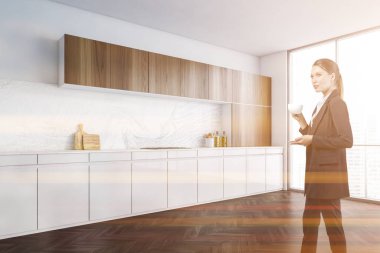 Çekici bir iş kadını gökdelen ofisindeki ya da iç mekandaki şirket mutfağında kahve içiyor. Modern mutfak seti ve tesisleri. Kafkas zarif modeli resmi olarak giyiniyor..