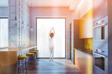 Mutfak seti, bar sandalyeli yemek masası, parke zemin, şehir manzaralı kadın. Lavabo ve fırınla açık uzay yemek odası, mercek renkli görüntü.