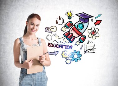 Beyaz tişörtlü, kot pantolonlu, elinde pano planlayıcısı olan ve üniversite mezuniyetini düşleyen genç bir kız. Arkaplanda eğitim skeci.