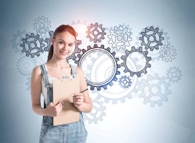 Beyaz tişörtlü ve kot pantolonlu genç bir kız elinde bir pano planlayıcısı tutuyor ve gelecekteki kariyer fırsatlarını hayal ediyor. Arka planda dişli tekerlek aralığı.