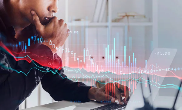 Black man sitting with device in office room in suit, pensive looking and analysing. Stock statistics hud, candlesticks changes on foreground