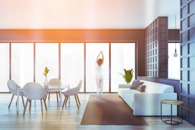 Ahşap ve gri mutfak odası içi, parke zeminde kadın, şehir manzaralı. Kanepeli açık bir oturma odası ve sandalyeli yemek masası, parlak mercekli görüntü.