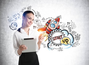 Beyaz tişörtlü, elinde elektronik aletle gülümseyen ofis müdürü kadın. Roket fırlatma simgeleri gri beton duvarda, yeni bir ürünün tanıtımı. Yeni proje ve iş fikirleri kavramı