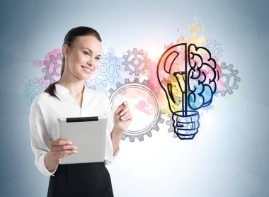 Elinde tablet olan bir iş kadını renkli beyin çizimi ve vitesli bir ampul. Mavi arka plan duvarında resim çizimi. Başlangıç ve yeni fikirler kavramı