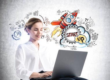 Beyaz gömlekli bir iş kadını dizüstü bilgisayarda çalışıyor. Roket, gri beton üzerine yeni bir ürün başlatma simgeleri. Yeni proje ve iş fikirleri kavramı