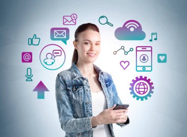 Kot ceketli, elinde akıllı telefonuyla gülümseyen bir öğrenci. Sosyal iletişim simgeleri, ağ konsepti, teknoloji ve arayüz