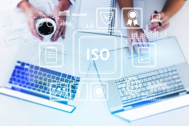 Dizüstü bilgisayarda çalışan ve uluslararası standartlar organizasyonunu araştıran iki iş kadınının üst görüşü, ISO kalite kontrol garantisi hologramı. İş teknolojisi kavramı