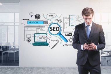 Takım elbiseli yakışıklı iş adamı elinde akıllı telefon tutuyor ve arama motoru optimizasyonunu merak ediyor. Arkadaki beton duvarda Seo simgeleri var. Projenin başlatılmasında başarı kavramı