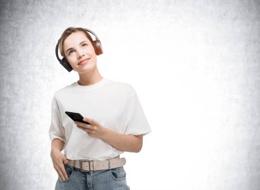 Beyaz bluz ve kot pantolon giyen bir kadın elinde akıllı bir telefon tutuyor ve başarılı bir girişim için yaratıcı fikirler üzerinde kafa yoruyor. Çağdaş sektörde artan genç nesil kavramı