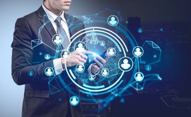 Resmi takım elbiseli bir iş adamı parmağıyla akıllı telefon ekranına dokunuyor. Önplanda insan kaynakları ikonlarının olduğu hologram. Takım çalışması ve işbirliği kavramı
